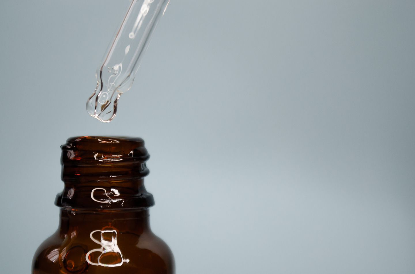 A glass dropper above an open amber bottle